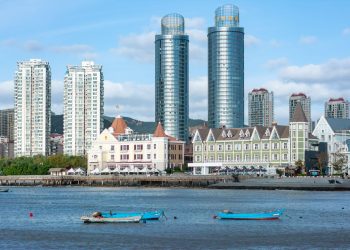 A stunning cityscape featuring modern high-rise buildings with a waterfront view and small boats.