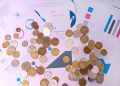 Image of various coins on financial documents with graphs and charts.