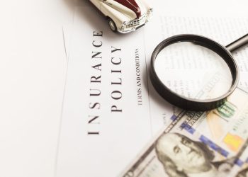 Close-up image of an insurance policy with a magnifying glass, money, and toy car.