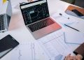 Laptops on a desk displaying stock market charts and financial documents.