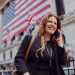 Smiling businesswoman using phone outside the stock exchange with flags in background.