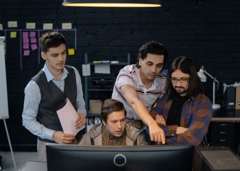 Group of professionals discussing a project at a computer in a modern office environment.
