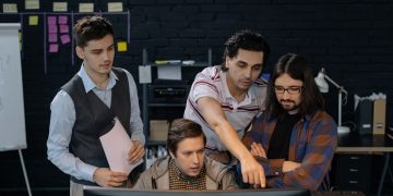Group of professionals discussing a project at a computer in a modern office environment.