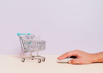 Conceptual image of a hand on a mouse next to a miniature shopping cart filled with ice cubes, symbolizing online shopping.