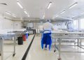 A person wearing protective clothing working in a bright, sterile laboratory environment.