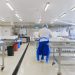 A person wearing protective clothing working in a bright, sterile laboratory environment.