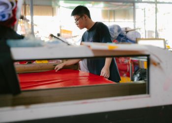 A focused worker examines fabric in a busy textile workshop.