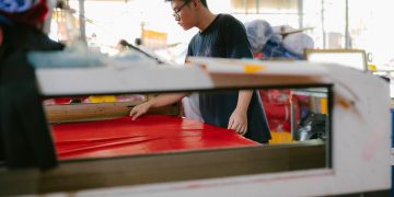 A focused worker examines fabric in a busy textile workshop.