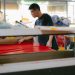 A focused worker examines fabric in a busy textile workshop.