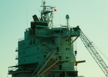 Close-up of an industrial ship's structure and crane against a sunset backdrop.