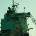 Close-up of an industrial ship's structure and crane against a sunset backdrop.