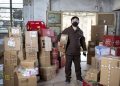 Delivery worker holding packages in a Wuhan warehouse, wearing a face mask.