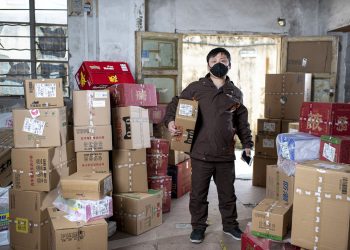 Delivery worker holding packages in a Wuhan warehouse, wearing a face mask.