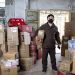 Delivery worker holding packages in a Wuhan warehouse, wearing a face mask.
