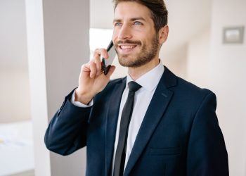 Confident businessman in suit making a phone call indoors, smiling.