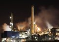 A nighttime view of an industrial factory with smokestacks emitting smoke, highlighting energy production and pollution.