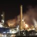 A nighttime view of an industrial factory with smokestacks emitting smoke, highlighting energy production and pollution.
