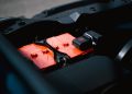 Detailed view of an orange car battery inside a vehicle's engine bay, highlighting its features.