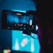 Close-up of a person filming a concert with a smartphone, capturing vibrant stage lights and atmosphere.