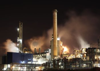 A nighttime view of an industrial factory with smokestacks emitting smoke, highlighting energy production and pollution.