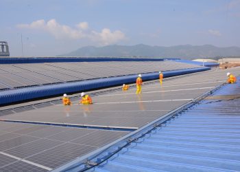 Workers installing solar panels on a large roof, highlighting renewable energy and sustainability.