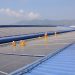 Workers installing solar panels on a large roof, highlighting renewable energy and sustainability.