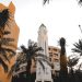 A striking clock tower surrounded by palm trees against a bright sky in an urban environment.