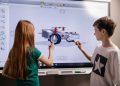 A boy and girl collaborate on a robotics project using a digital screen in a classroom setting.