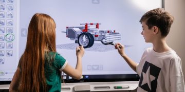 A boy and girl collaborate on a robotics project using a digital screen in a classroom setting.