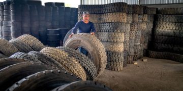 Man organizing large industrial tires in a warehouse, showcasing labor and storage setup.