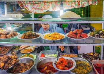 Colorful Indonesian street food stall with a variety of traditional dishes and a vendor serving customers.