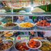 Colorful Indonesian street food stall with a variety of traditional dishes and a vendor serving customers.