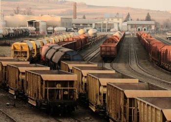 A busy freight train yard with multiple tracks and a variety of train cars in a rural setting.