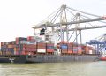 Cargo vessel moored at Kochi, Kerala, India, showcasing global container shipping with cranes in background.