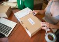 Two people packing online orders in a small business setting with a laptop.