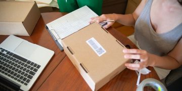 Two people packing online orders in a small business setting with a laptop.