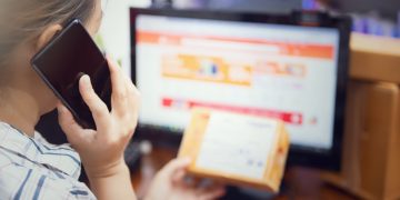 Woman multitasking by using a phone and checking an online purchase package at home.
