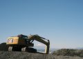 Excavator at work on a construction site, with a scenic mountain backdrop under clear skies.