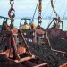 Heavy machinery loading coal at a port with a clear sky reflecting on the water.