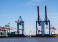 Cranes at the busy Hamburg harbor with blue skies and wind turbines.