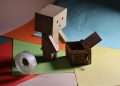 Charming cardboard figurine on colorful paper with a wooden box and tape. Ideal for crafting themes.
