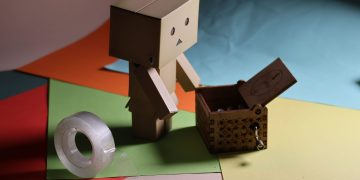 Charming cardboard figurine on colorful paper with a wooden box and tape. Ideal for crafting themes.
