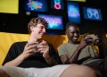 Two happy young men sitting together enjoying mobile gaming indoors.